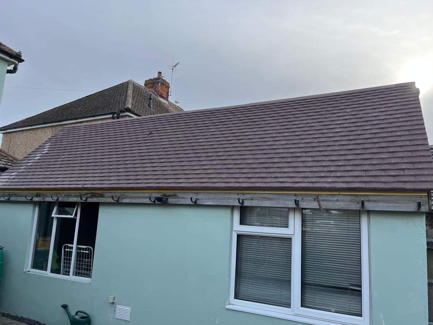 Completed dark-tiled roof on a rendered bungalow